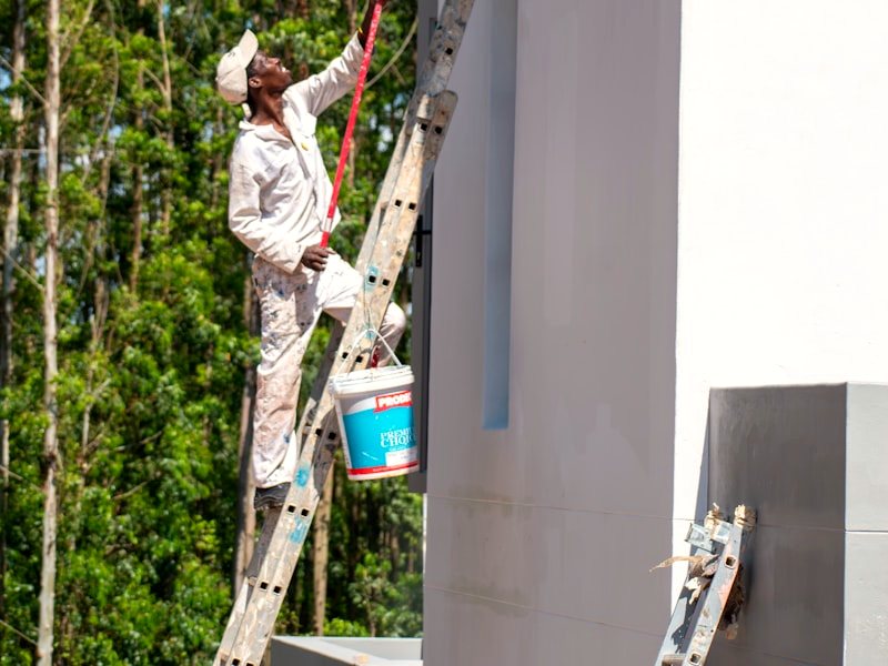 A painter on a ladder working the exterior of a house